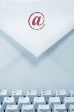 Briefumschlag mit @-Symbol auf dem Papier und einer Computertastatur im Vordergrund.