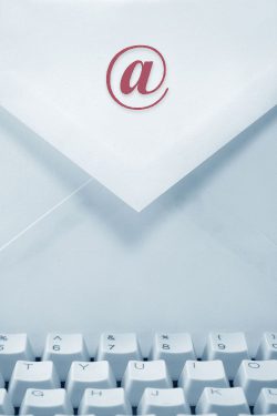 Briefumschlag mit @-Symbol auf dem Papier und einer Computertastatur im Vordergrund.